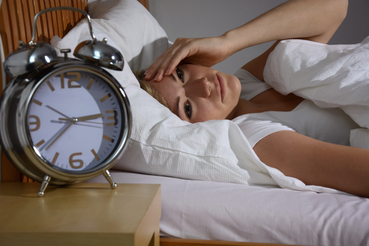 Eine Frau mit Schlafproblemen liegt im Bett und schaut auf ihren Wecker.