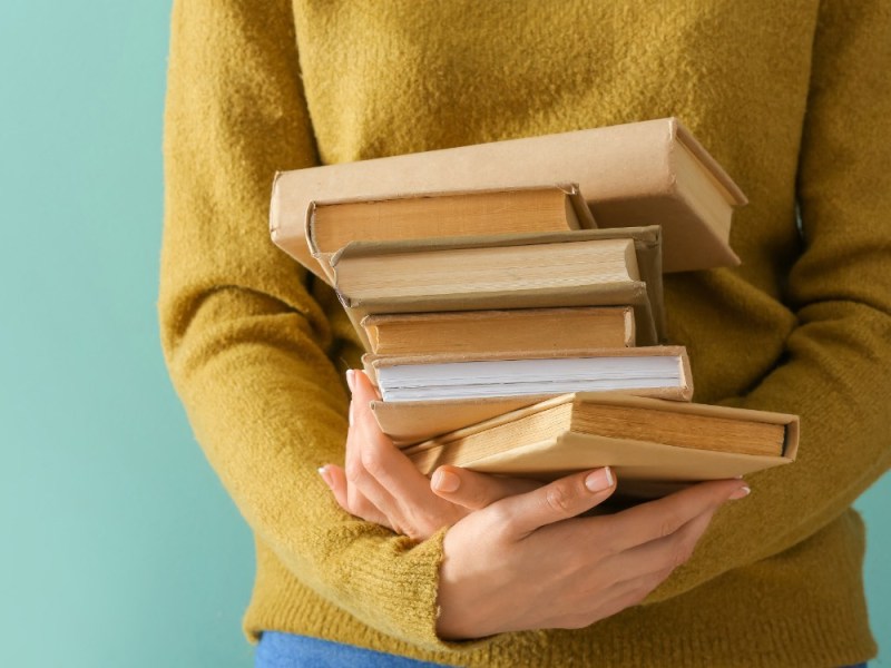 Eine junge Frau hÃ¤lt einen Stapel BÃ¼cher in den HÃ¤nden.