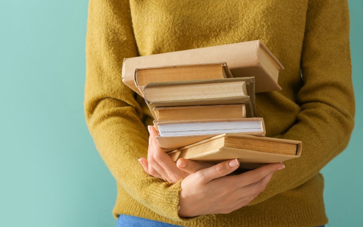 Eine junge Frau hält einen Stapel Bücher in den Händen.