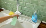 Ein Hausmittel gegen Schimmel wird aus einer Sprühflasche an eine grün gekachelte Küchenwand gesprüht.