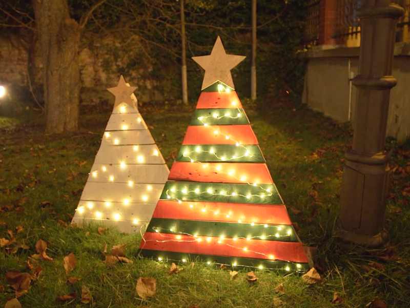 Zwei aus Paletten gebastelte Weihnachtsbäume stehen abends in einem Garten, von Lichterketten erleuchtet.