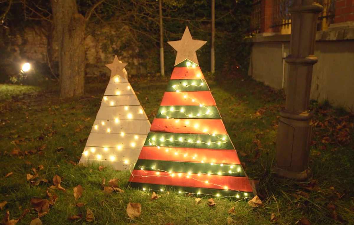 Zwei aus Paletten gebastelte Weihnachtsbäume stehen abends in einem Garten, von Lichterketten erleuchtet.