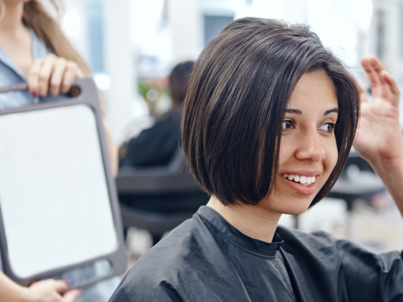 Eine Frau mit Bob-Frisur betrachtet ihr Haar beim Friseur.