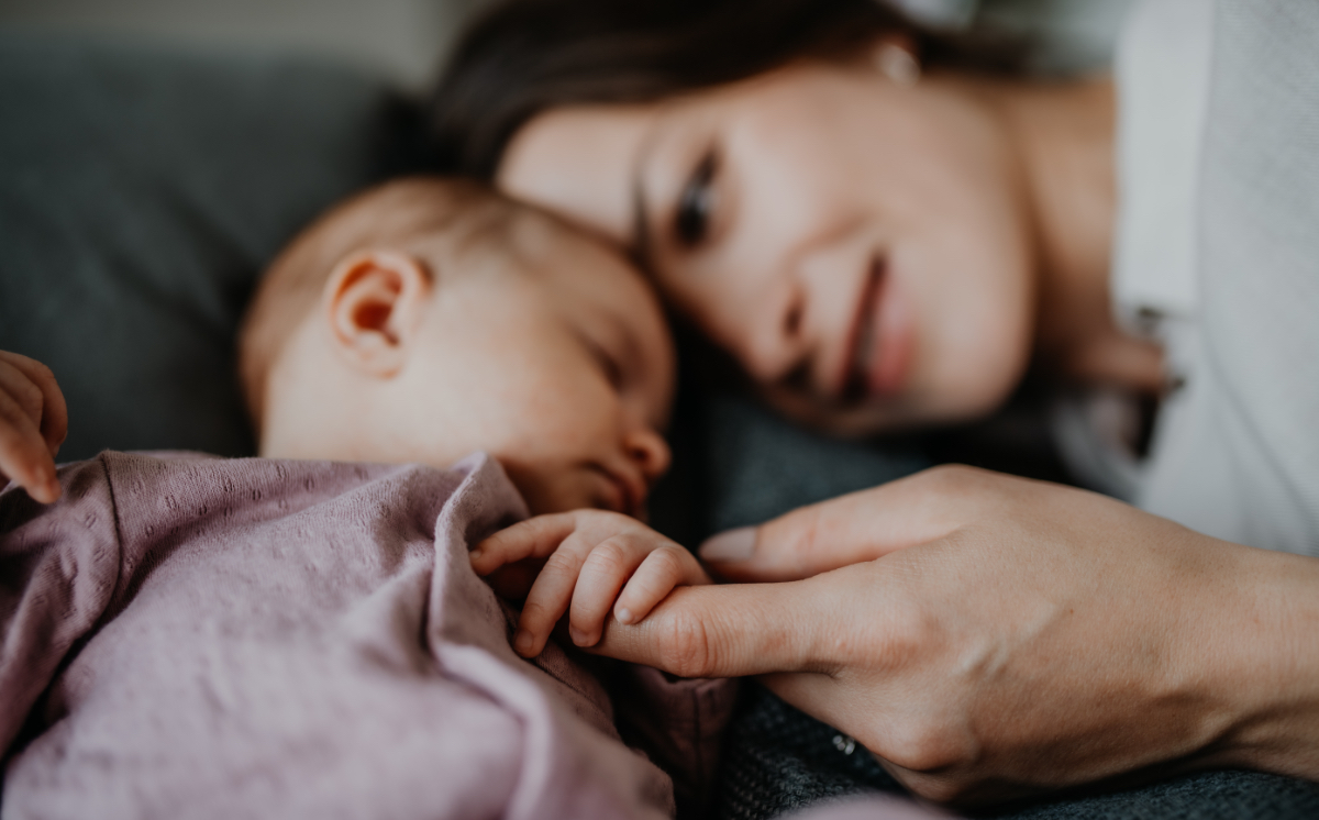 Eine glückliche junge Mutter liegt neben ihrem schlafenden Baby.