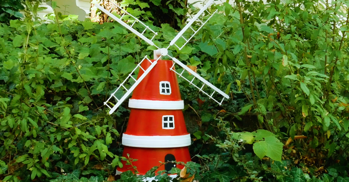 Eine Deko-Windmühle, aus Blumentöpfen gebastelt, steht in einem Garten.