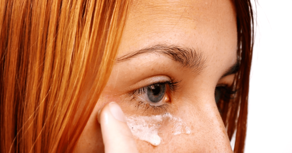 Eine junge Frau mit roten Haaren trägt sich Kaffeesatz unter den Augen auf.