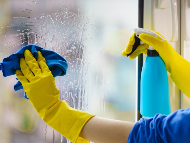 Eine Person putzt mit gelben Handschuhen und Lappen ein Fenster.