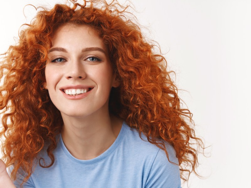 Eine rothaarige Frau mit Locken lächelt in die Kamera.