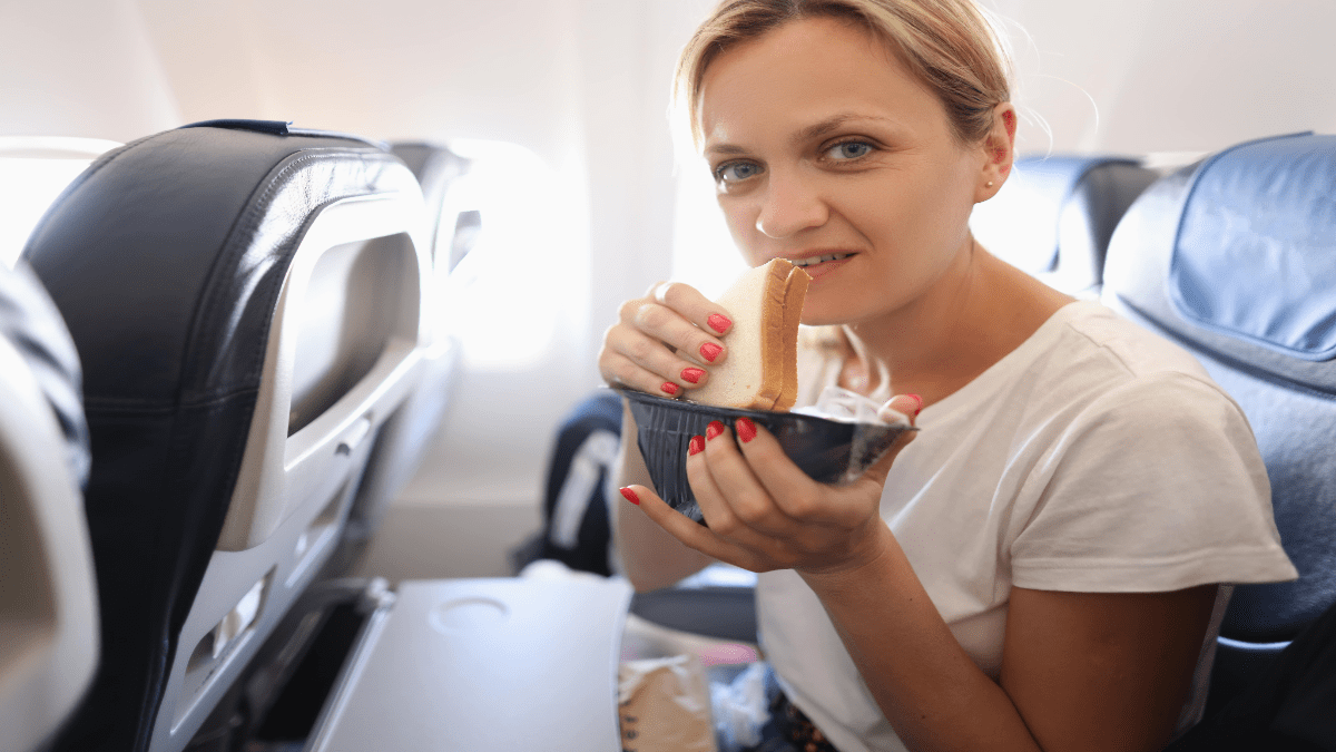 Frau guck fragend in die Kamera während sie ein Sandwich isst.