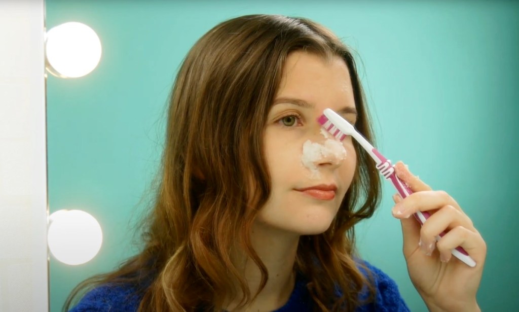 Eine junge Frau reinigt sich die Haut mit einem Backpulver-Peeling und einer Zahnbürste.