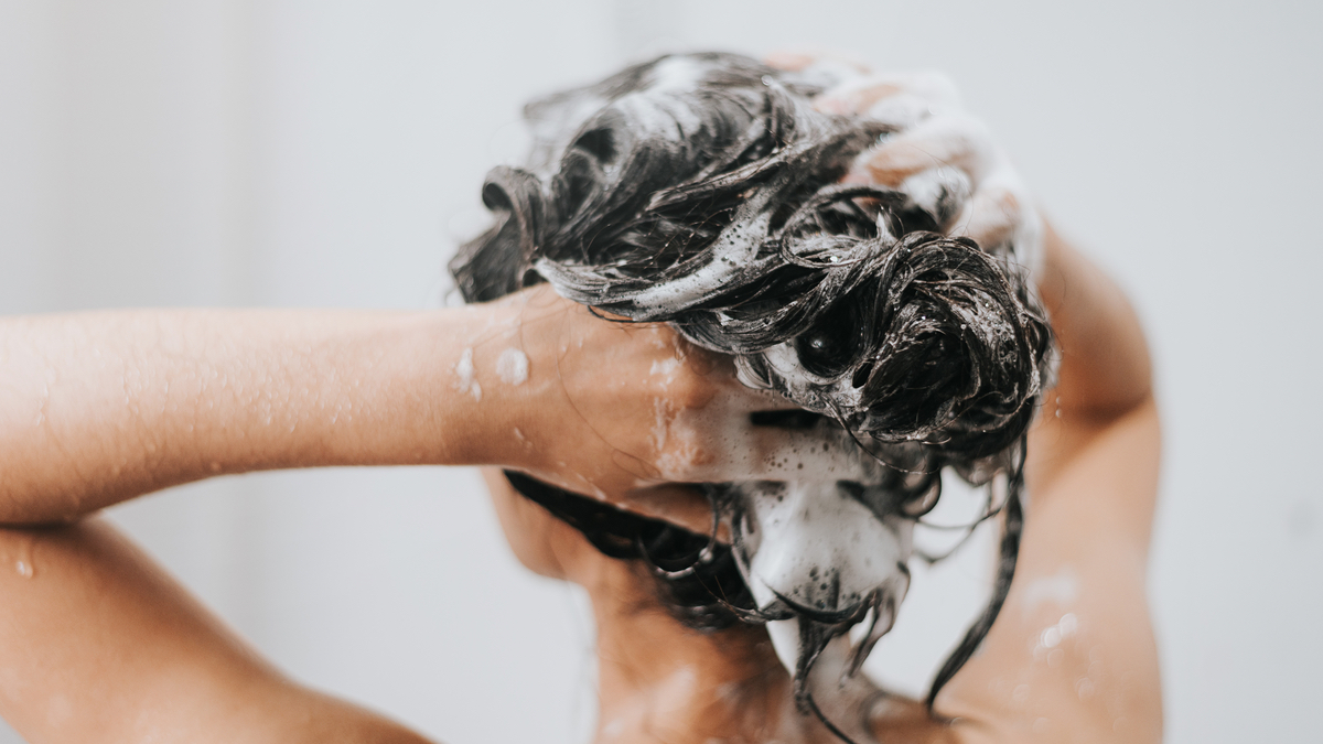 Eine Frau, die ihre Haare mit Shampoo einschäumt.