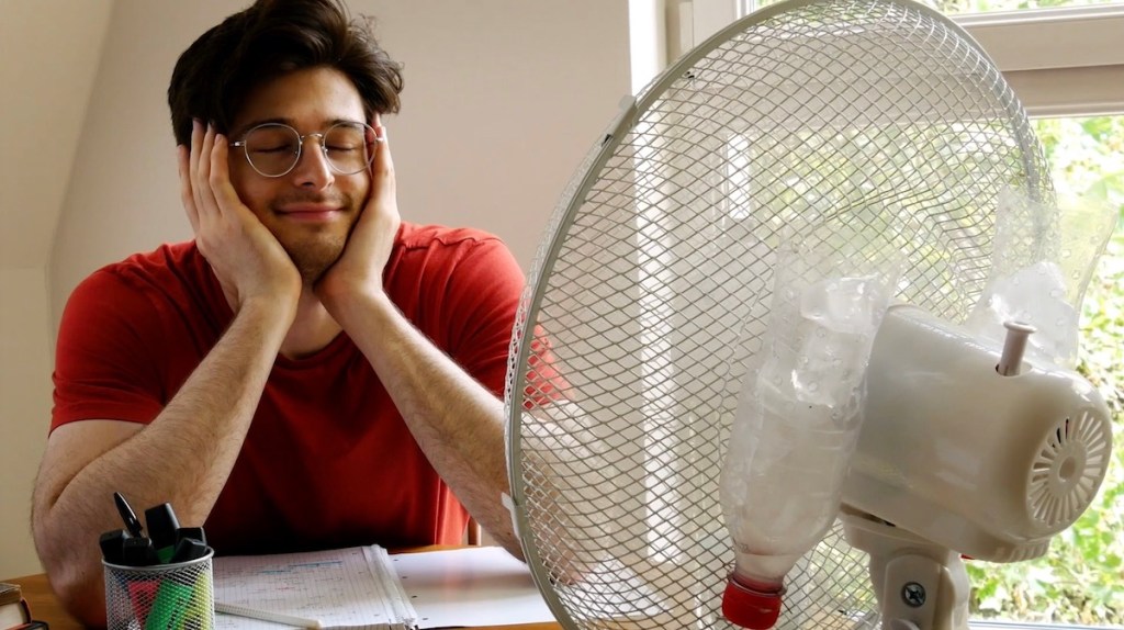 Ein Mann sitzt glücklich vor einem laufen Ventilator.