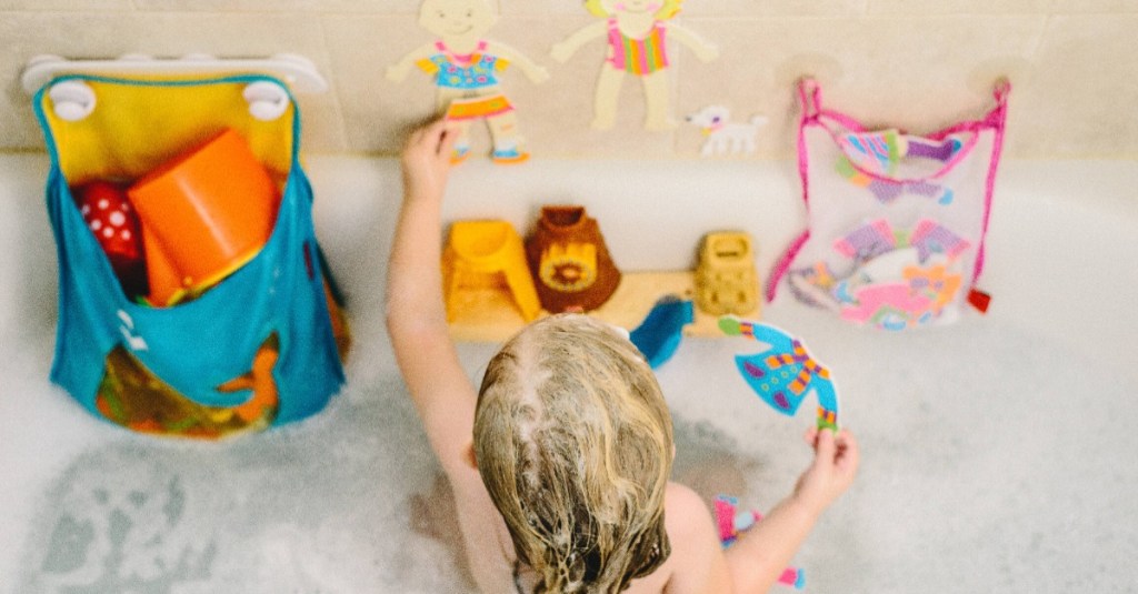 kleines Mädchen sitzt in der Badewanne und spielt mit Badespielzeug