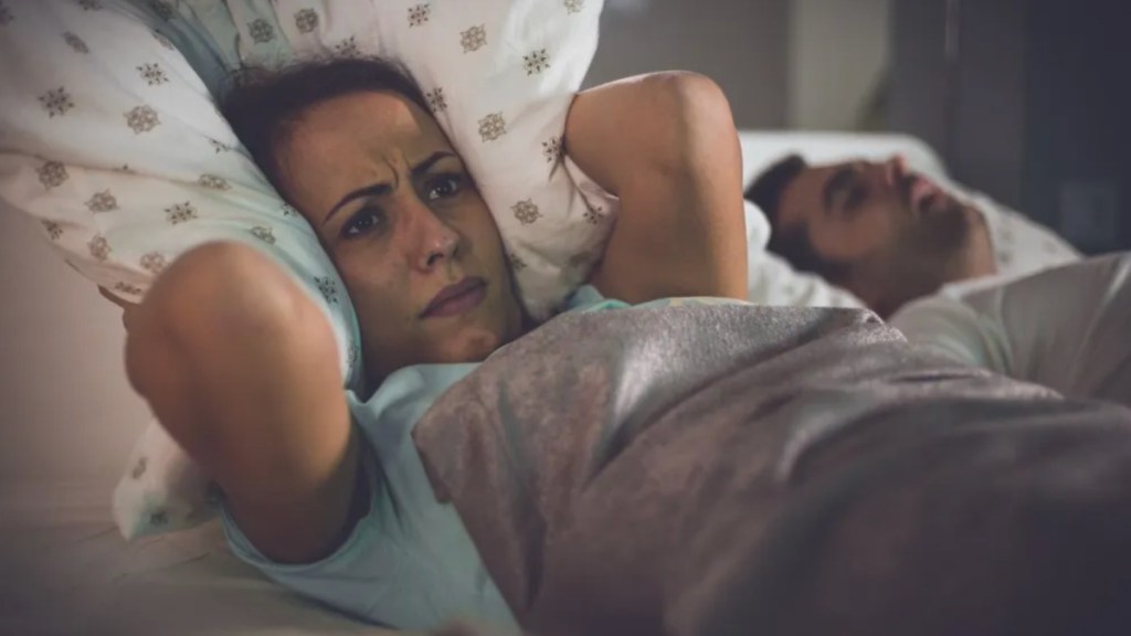 Frau und Mann liegen im Bett und die Frau hält sich ihr Kissen auf die Ohren