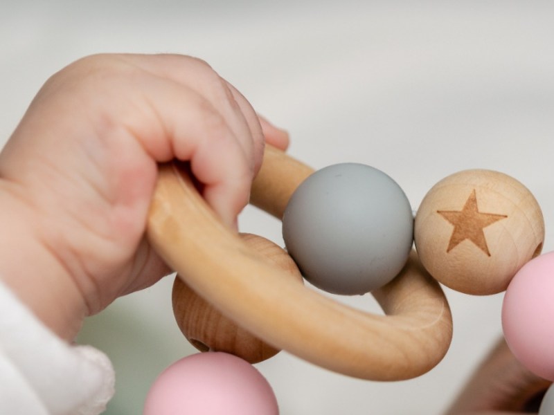 unnÃ¶tige Produkte fÃ¼r Kinder: eine Babyhand greift nach einem Holzring