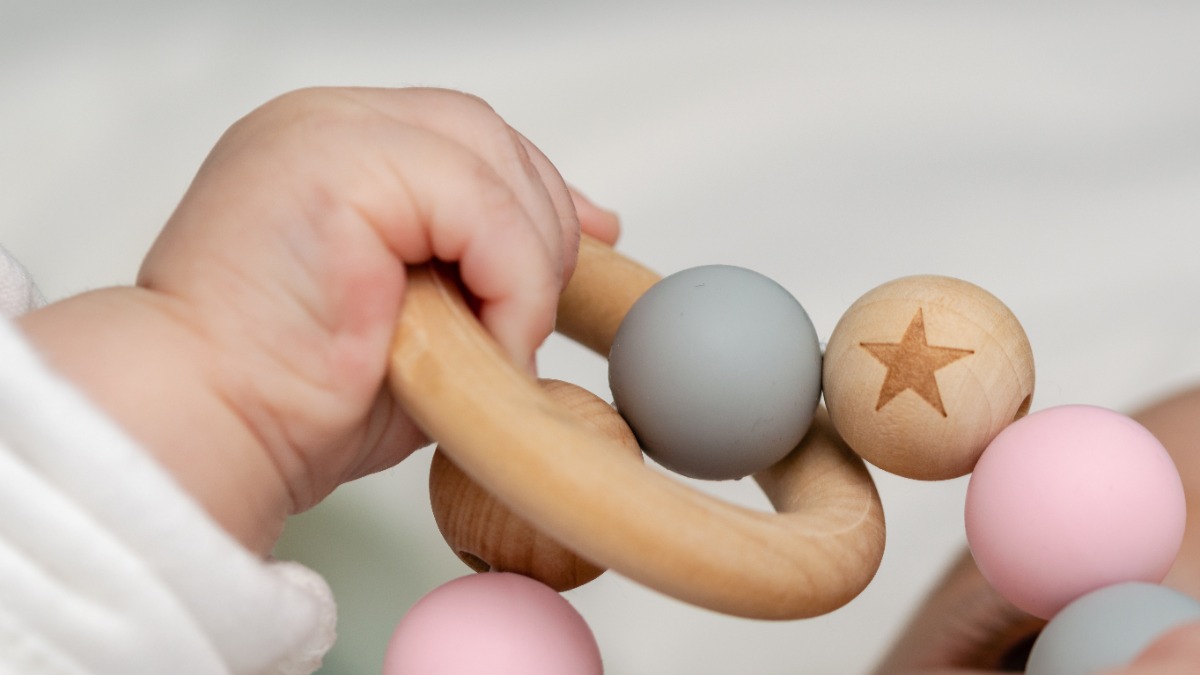 unnÃ¶tige Produkte fÃ¼r Kinder: eine Babyhand greift nach einem Holzring