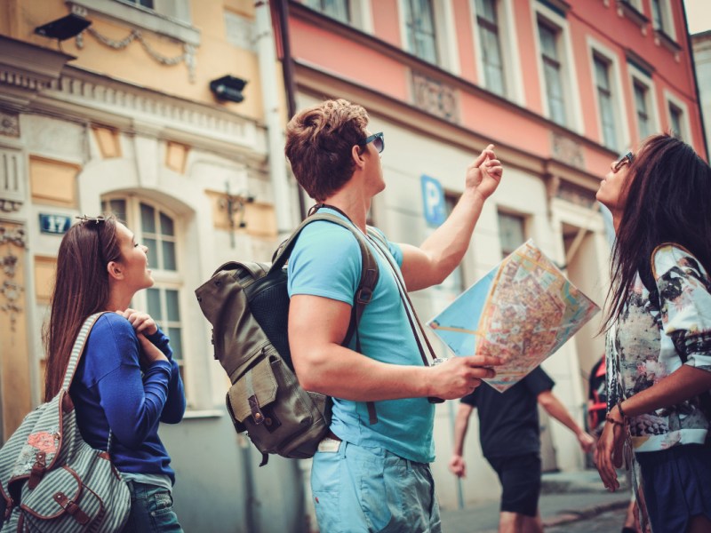 Drei junge Touristen stehen mit einer Karte in einer Altstadt.