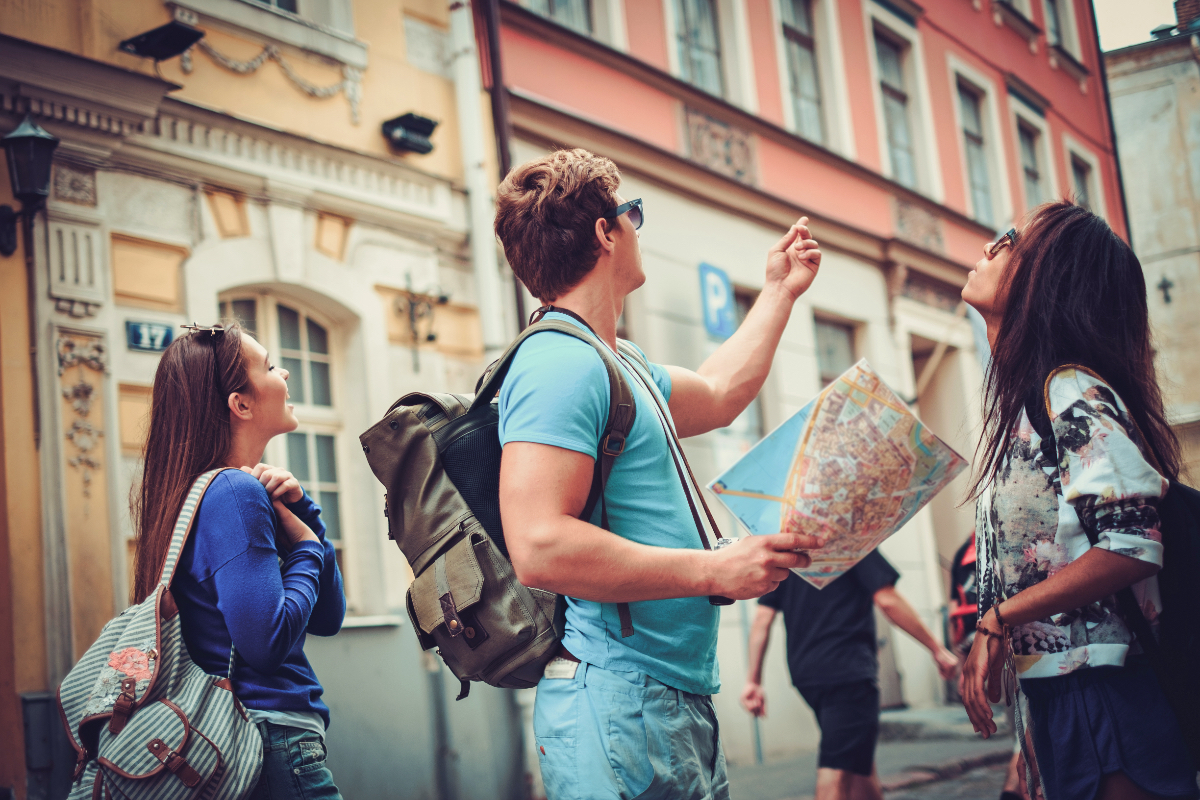 Drei junge Touristen stehen mit einer Karte in einer Altstadt.