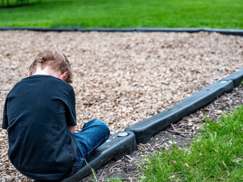 Kind sitzt alleine auf einem Spielplatz