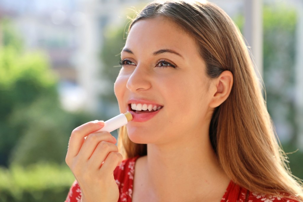 Eine lächelnde junge Frau benutzt einen Lippenbalsam-Stift.