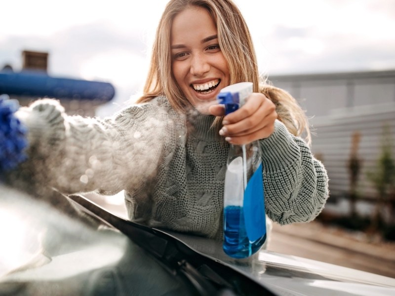 Frau putzt Autoscheibe.