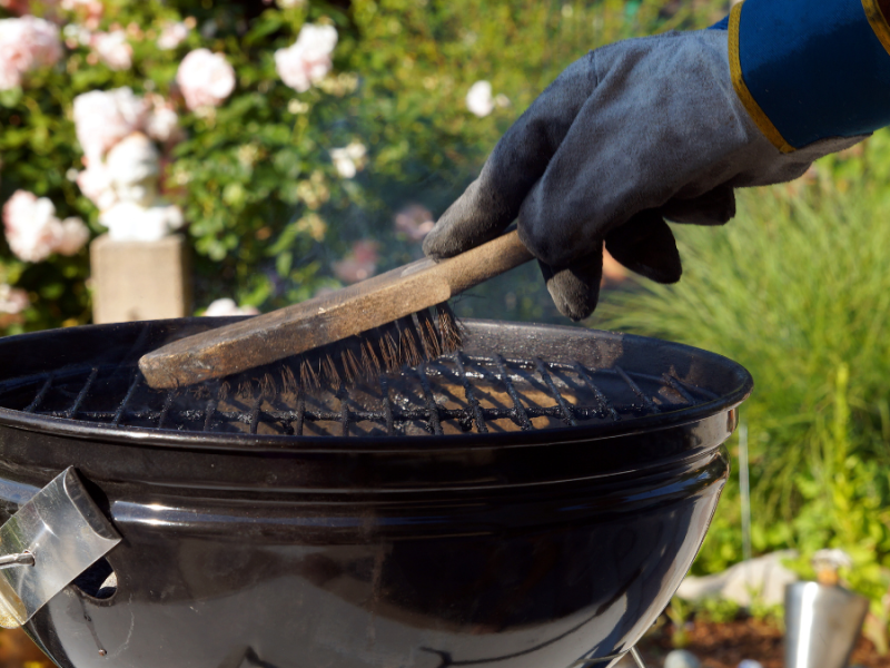 Eine Person reinigt einen Grill mit einer Bürste.