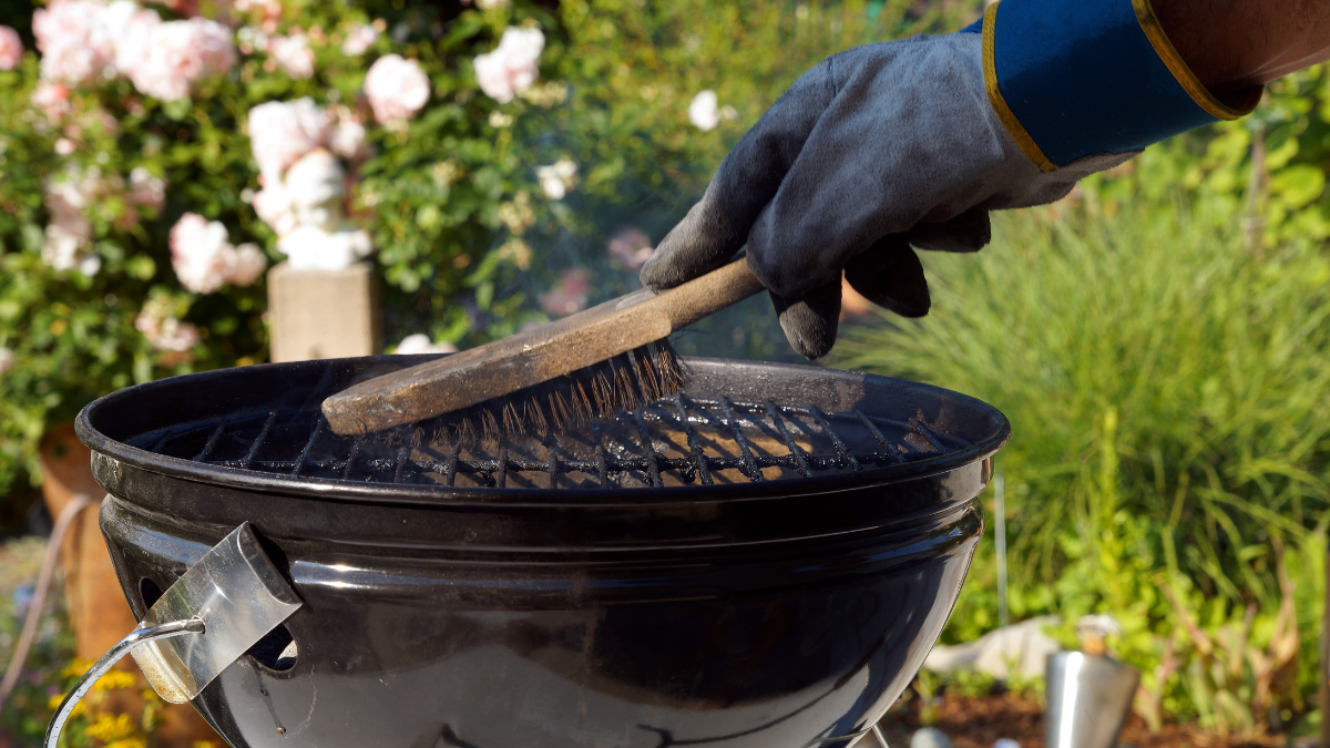 Eine Person reinigt einen Grill mit einer Bürste.