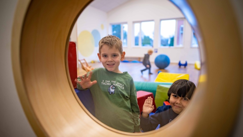 Kinder winken durch ein Bullauge im Kindergarten