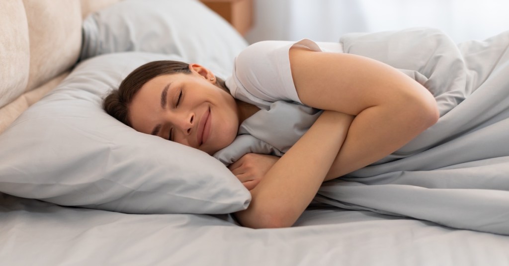 Frau liegt im Bett und umarmt glücklich ihre Bettdecke.