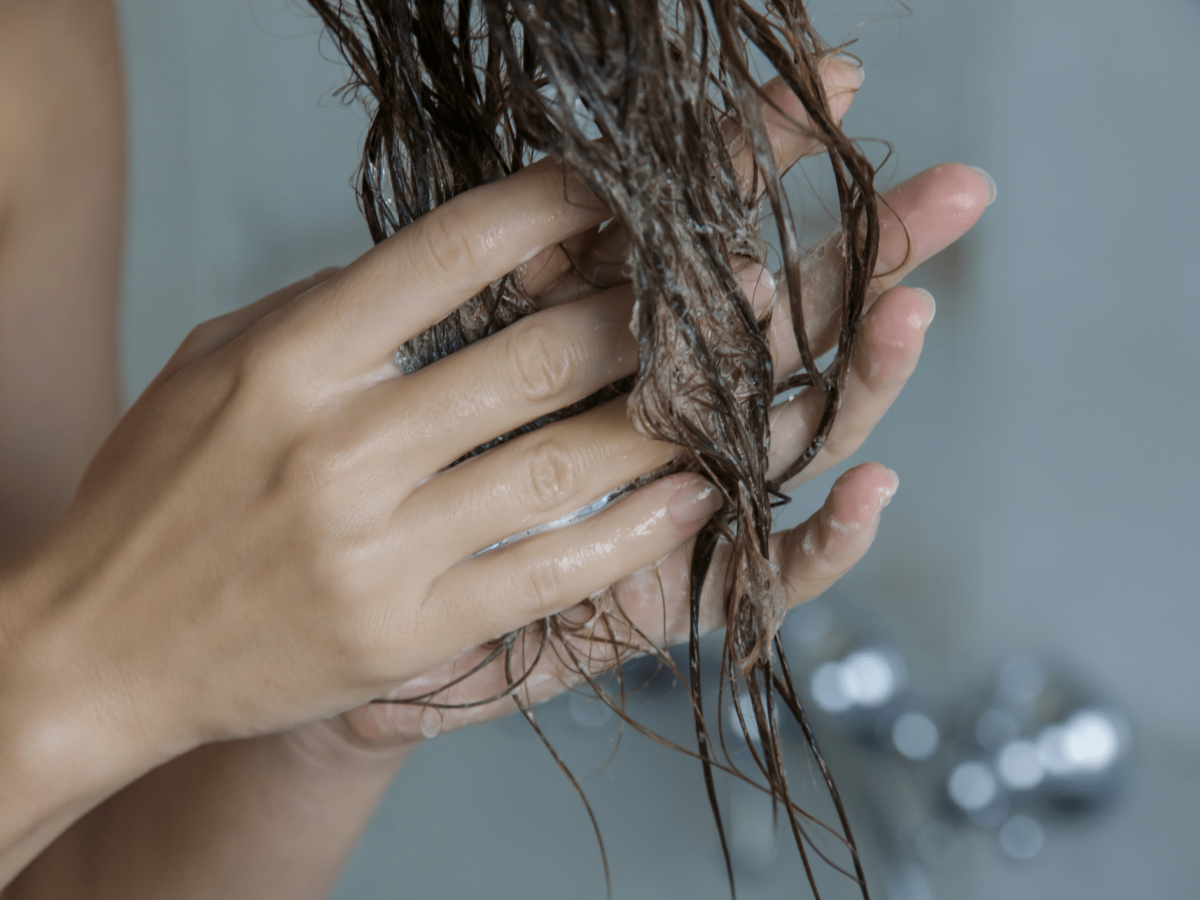 Eine Frau knetet Conditioner in ihre Haarspitzen ein.