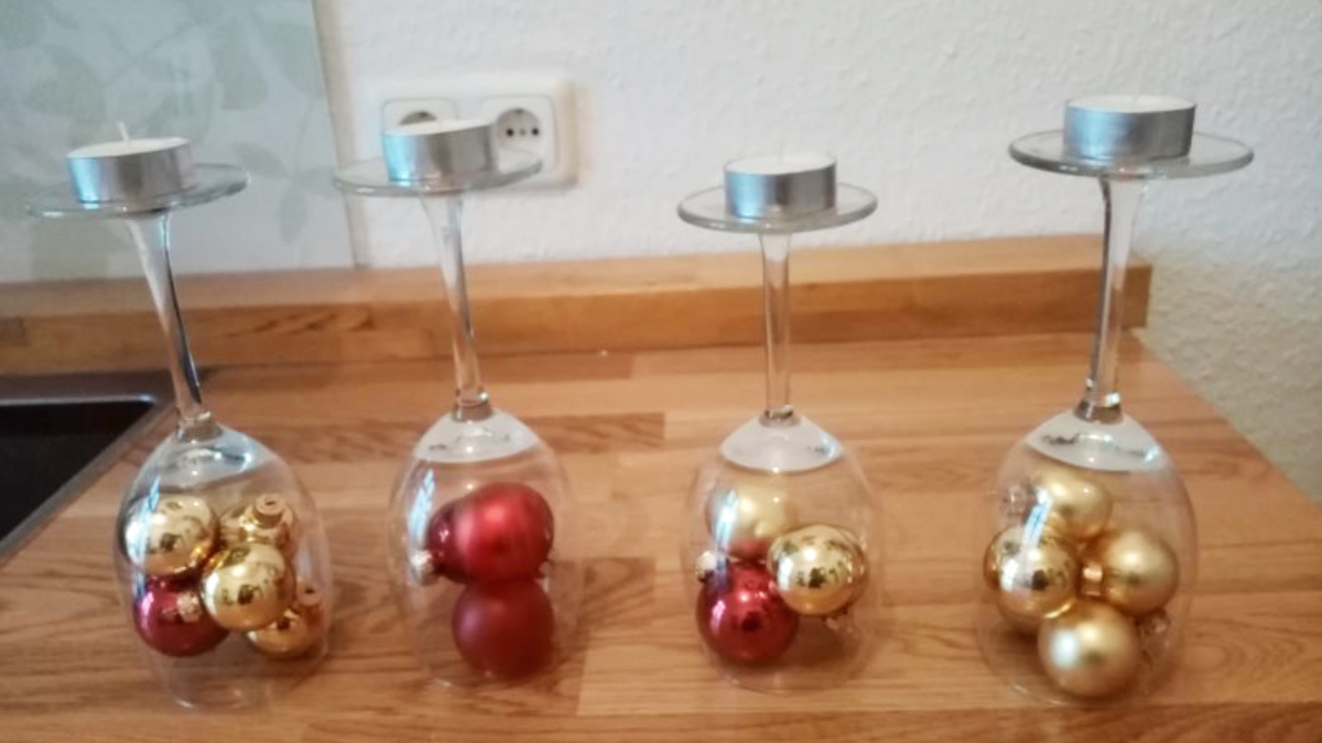 Ein Weihnachtskranz-Gesteck aus Christbaumkugeln in umgedrehten Weingläsern.