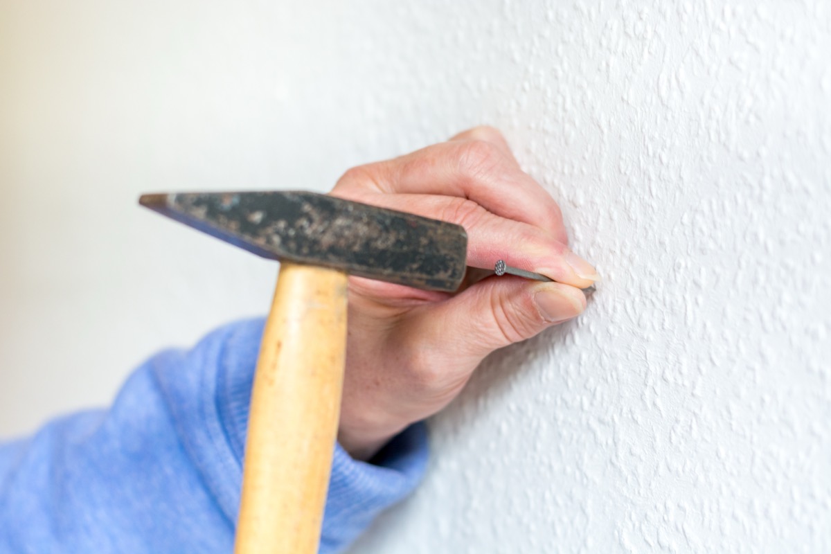 Ein Mann hämmert mit einem Hammer einen Nagel in eine Wand.