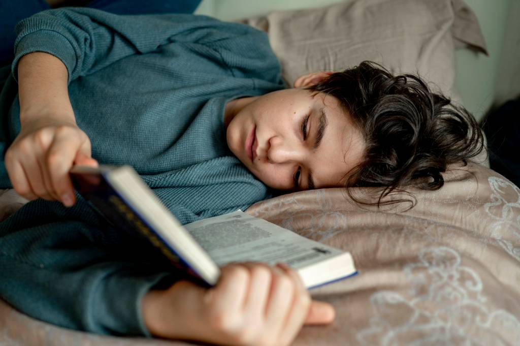 Junger Mann liest ein Buch im Bett.