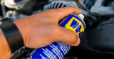 Eine Hand hält eine Dose WD-40 über eine verrostete Stelle
