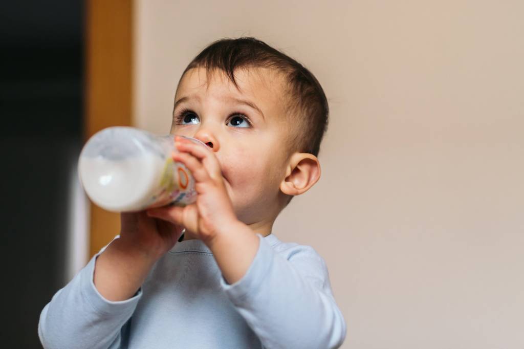 Kind trinkt Milch aus Flasche.