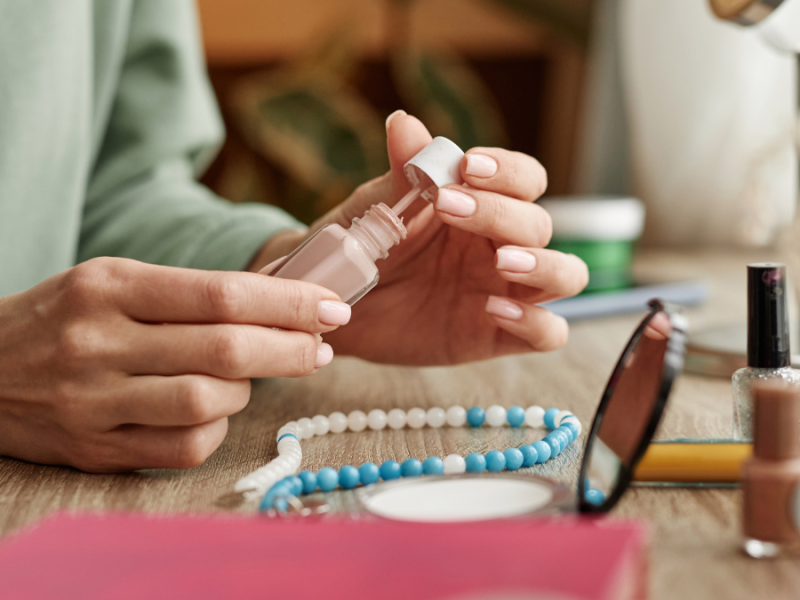 Eine Frau lackiert ihre Fingernägel mit hellem Nagellack.