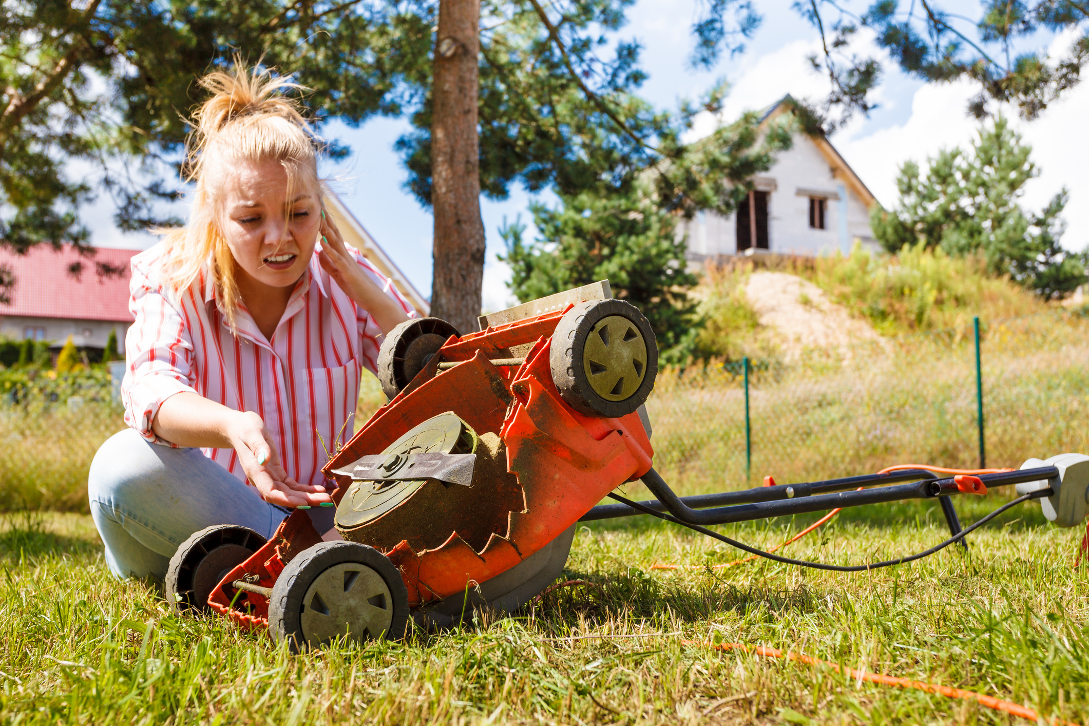 Frau im Garten sitzt verzweifelt vor kaputtem Rasenmäher