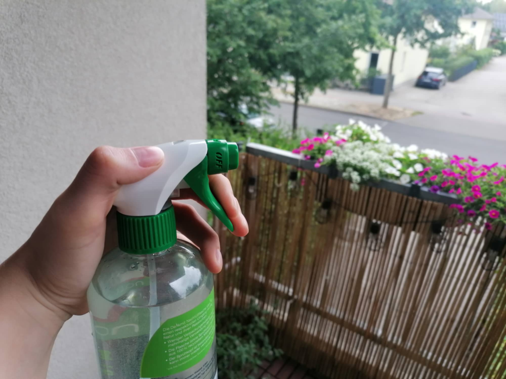 Jemand hält eine Sprühflasche in der Hand, um Wespen auf dem Balkon zu vertreiben.