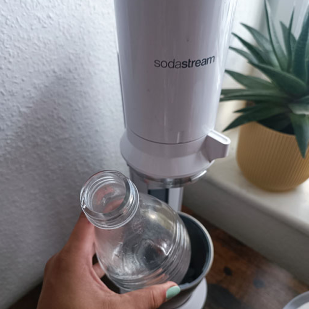 Eine Hand hält die Glasflasche eines SodaStream-Geräts.