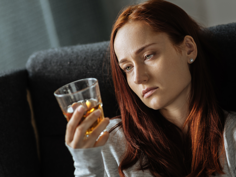 Traurige Frau überlegt, ein Glas Alkohol zu trinken.