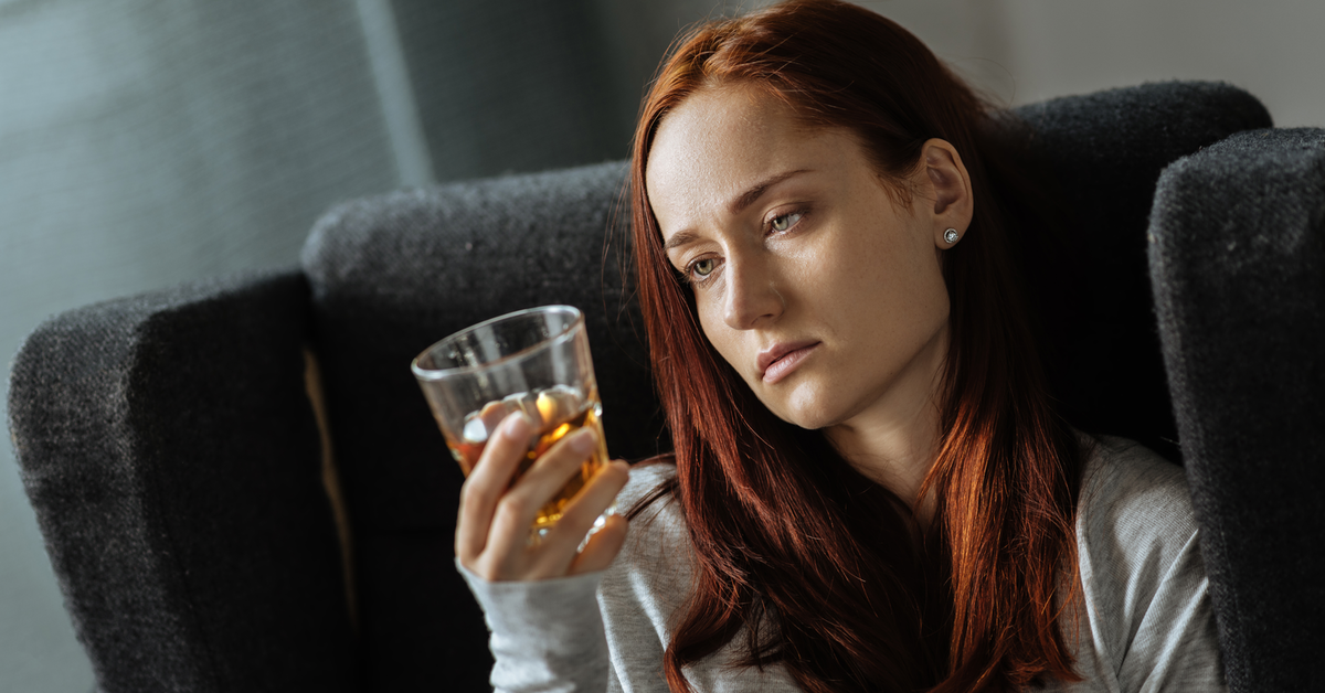 Traurige Frau überlegt, ein Glas Alkohol zu trinken.