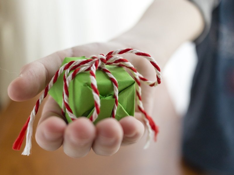 Eine Frau hält ein kleines, grünes Geschenk mit Schleife in der Hand.