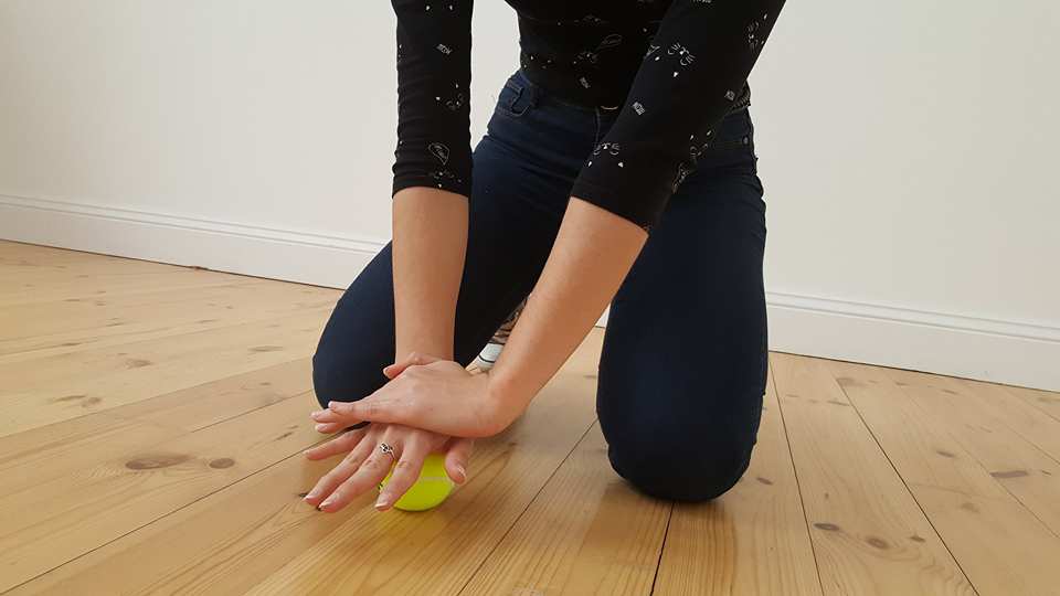 Eine Frau massiert sich die Hand mit einem Tennisball.