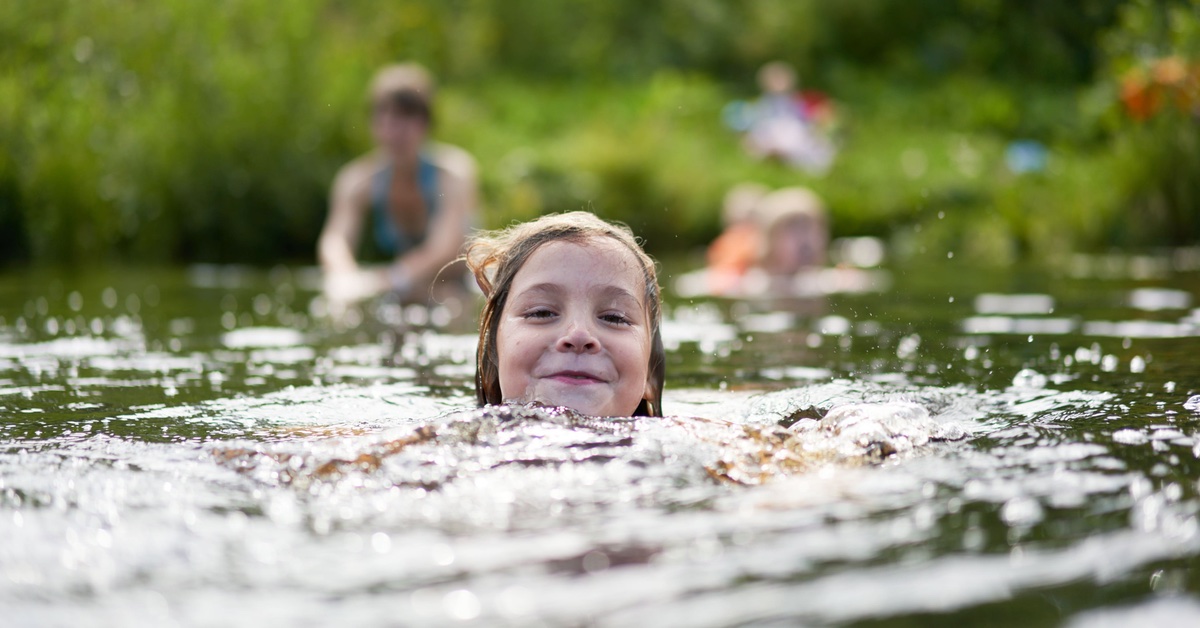 Ein junges Mädchen schwimmt lachend im Wasser.