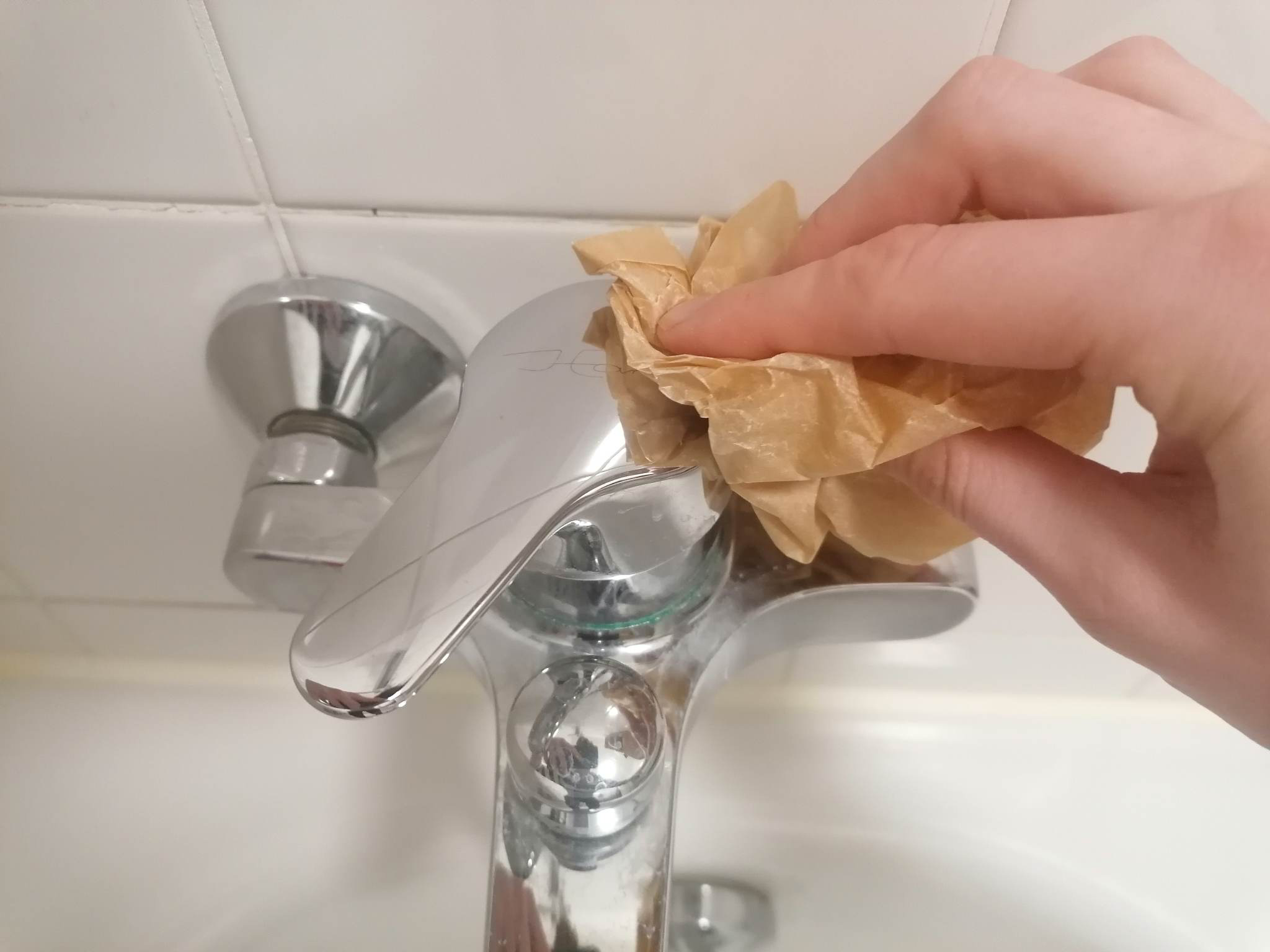 Jemand putzt mit etwas Backpapier einen Wasserhahn, um Kalk zu entfernen.