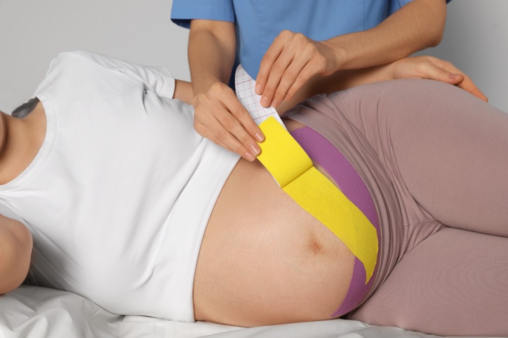 Eine schwangere Frau wird am Bauch mit Kinesio-Tape behandelt.