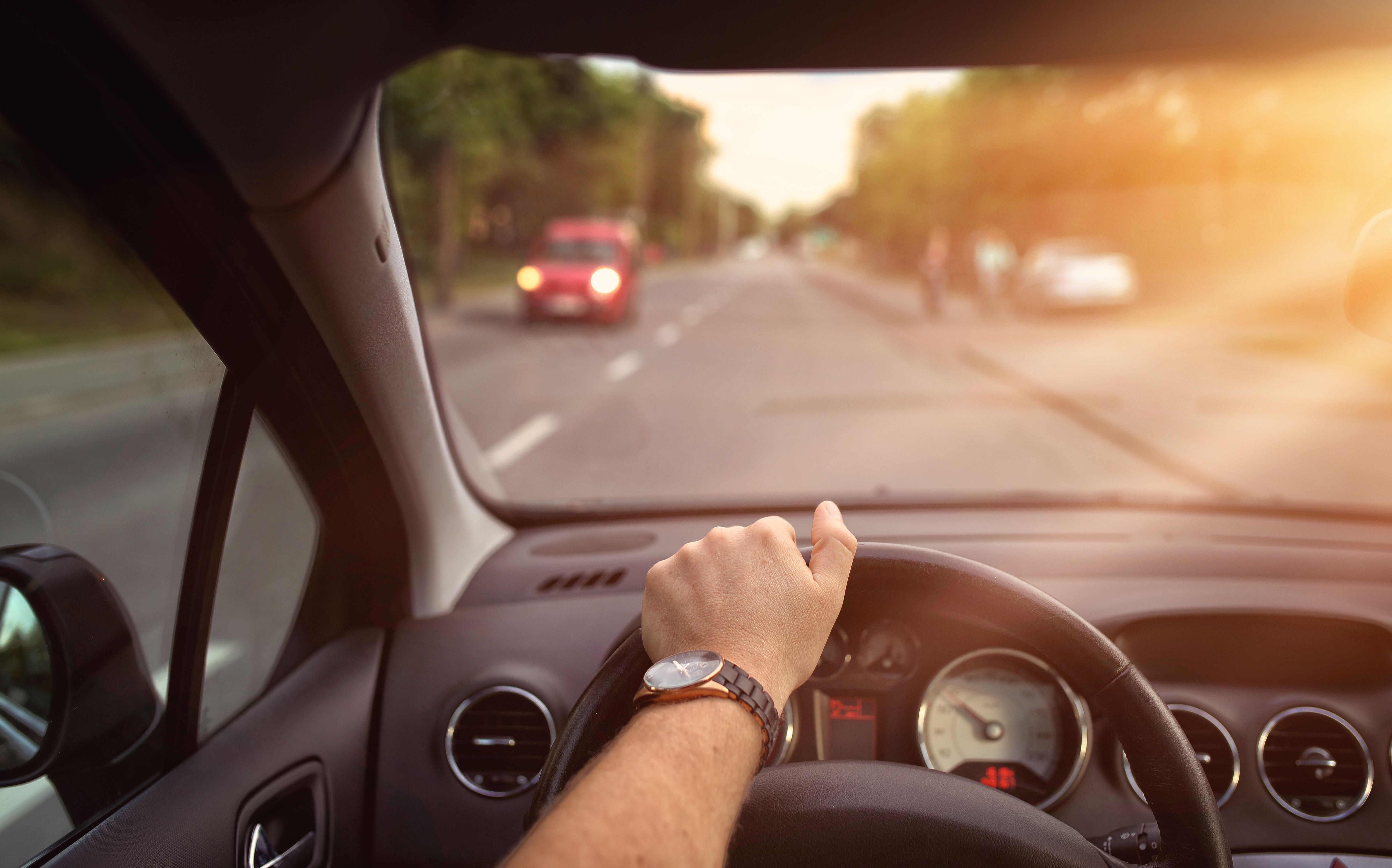 Hand am Lenkrad eines Autos, Sonnenlicht strahlt herein.