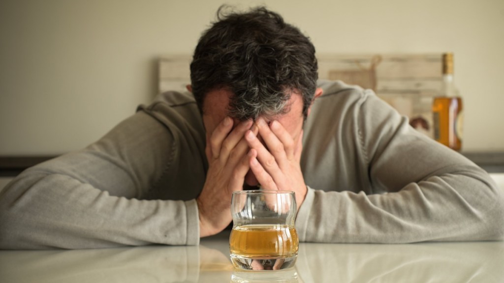 Mann sitzt verzweifelt vor einem Glas mit Alkohol.