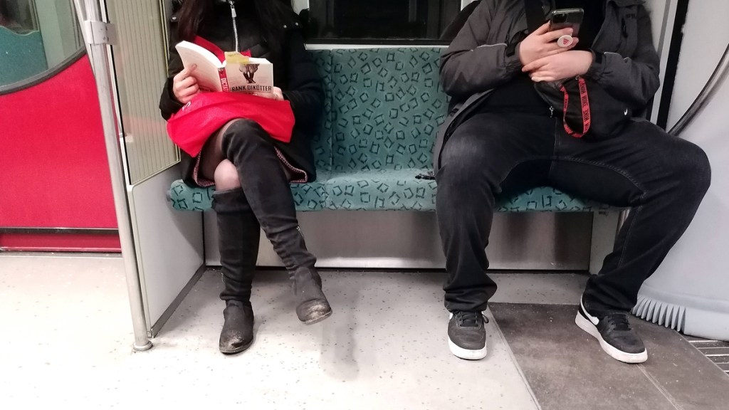 Frau und Mann sitzen in einer S-Bahn – auf ganz unterschiedliche Art und Weise.