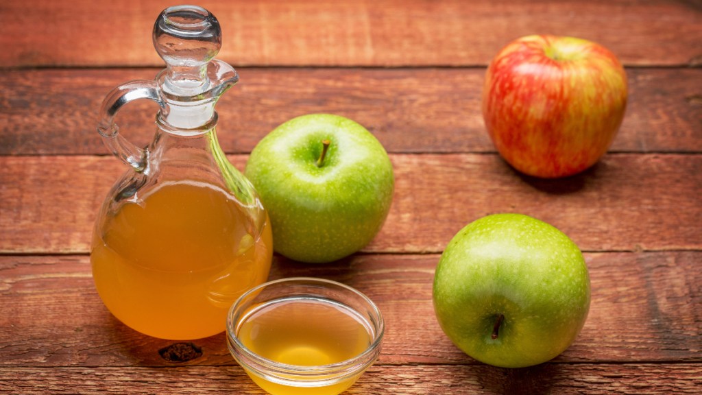 Ungefilterter, Apfelessig in einer Flasche, neben der drei Äpfel liegen.